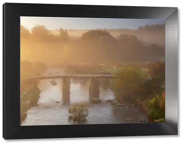 A clapper Bridge across the East Dart river in early morning mist, Dartmoor National Park, Devon, UK. October, 2018