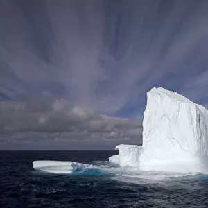 Huge iceberg with streaked sky under expansive open sky