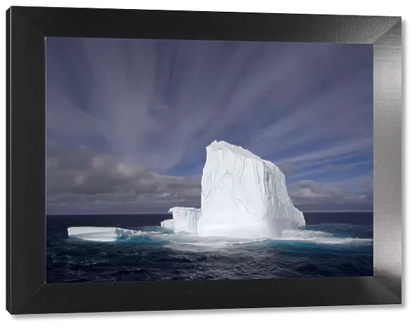 Huge iceberg with streaked sky under expansive open sky