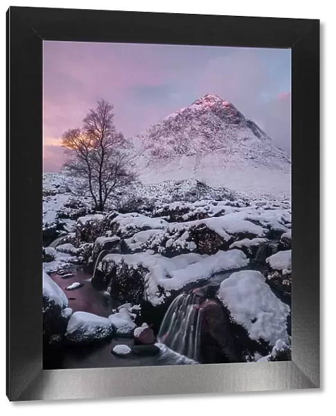 Pink sky at sunrise over a snow-covered landscape and highland stream, with a view to Buachaille Etive Mor, Glencoe, Scotland. November, 2017