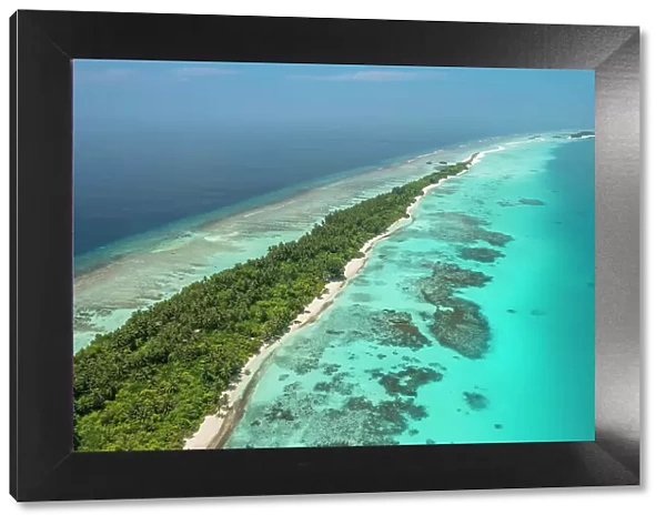 Aerial view of narrow coral atoll island with palm trees and white sand beach surrounded by reef, Dhigurah Island, South Ari Atoll, Maldives, Indian Ocean. February, 2020