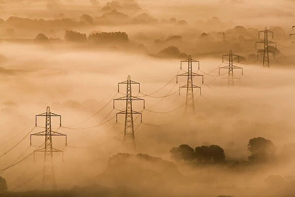 Electricity pylons rising through mist at dawn, view of The Marshwood Vale from Lambert s