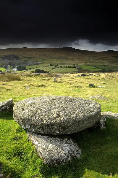 Hut circle remains and large circular granite slab, against stormy sky, Merrivale