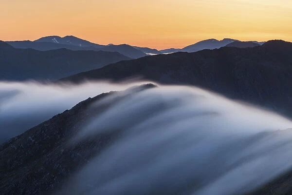 Long exposure of mist flowing over Bhudhie Bheinn at dawn with the mountains of Kintail