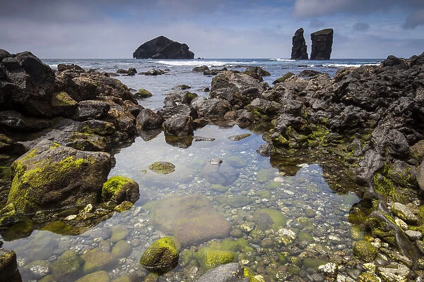 Rock pool in volcanic rock. Sea stacks and island in background