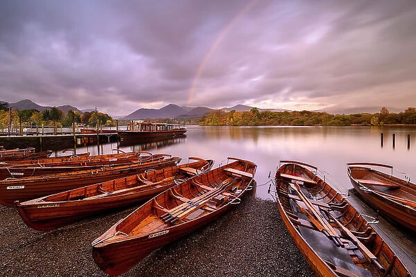 Rowing boats and jetties along the shore of Derwentwater, morning light and rainbow, Keswick, Cumbria, The Lake District, UK. October 2019