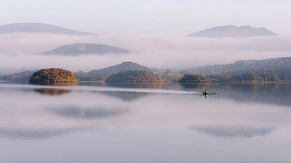 View over Derwentwater, towards Friars Crag in autumn colour and morning mist with lone rower. Near Keswick, The Lake District, Cumbria, UK. November 2016