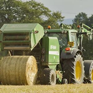 Baling machine ejecting a bale of Barley straw on arable farmland, Scotland, UK