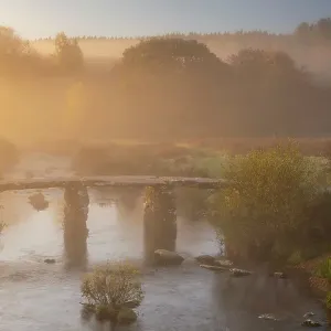 A clapper Bridge across the East Dart river in early morning mist, Dartmoor National Park, Devon, UK. October, 2018 A clapper Bridge across the East Dart river in early morning mist, Dartmoor National Park, Devon, UK. October, 2018