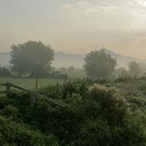 Glastonbury Tor, distant at misty early morning, with River Brue and meadows of the Somerset Levels