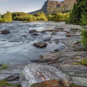 Der Fluss Hemsila im Sommer mit Bäumen umgebenen Ufer und Berge mit hohen Wolken am Horizont; Region Hemsedal, Norwegen; Juni 2022 Der Fluss Hemsila im Sommer mit Bäumen umgebenen Ufer und Berge mit hohen Wolken am Horizont; Region Hemsedal, Norwegen; Juni 2022