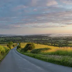 The road to Okeford Fitzpaine; dawn on Midsummers Day, in the Blackmore Vale, from Okeford Hill, Dorset, England, UK. June 2019 The road to Okeford Fitzpaine; dawn on Midsummers Day, in the Blackmore Vale, from Okeford Hill, Dorset, England, UK. June 2019