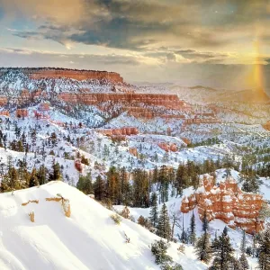 A snow bow forming over the snow-covered red sandstone hoodoos and geological formations in a high desert habitat during a winter sunrise, Bryce Canyon National Park, Utah, USA
