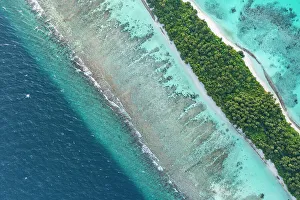 July 2023 Highlights Prints: Aerial view of narrow coral atoll island with palm trees and white sand beach surrounded by reef