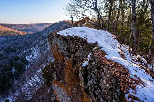 Sergey Gorshkov Prints: Amur leopard (Panthera pardus orientalis) standing on snow covered rocky outcrop with forested valley behind