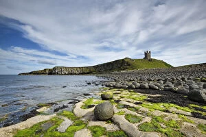 Exploring Britain Gallery: Dunstanburgh Castle on headland of the Whin Sill, eroded dolerite boulders in foreground