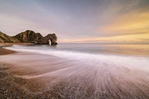 Durdle Door rock arch with beach in foreground, in evening light. Dorset, England, UK