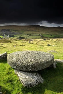 Hut circle remains and large circular granite slab, against stormy sky, Merrivale