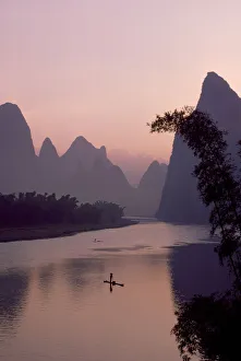Tranquil Scene Prints: Man using pole to propel bamboo raft on Lijang / Li River, Karst peaks beyond. At dawn