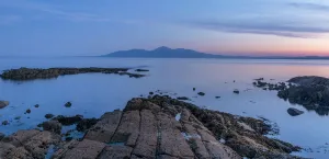 Rocky shore on St John's Point at sunset, mountains in distance across sea Rocky shore on St John's Point at sunset, mountains in distance across sea