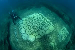 Scuba diver exploring splendid ancient Roman tessellatum mosaic in black and white decorated with pattern of hexagons