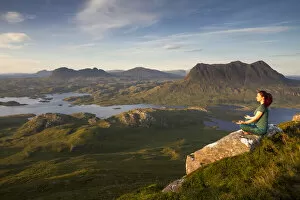 Woman meditating on Stac Pollaidh mountain with views of surrounding lochs and mountains, Assynt, Scotland, UK